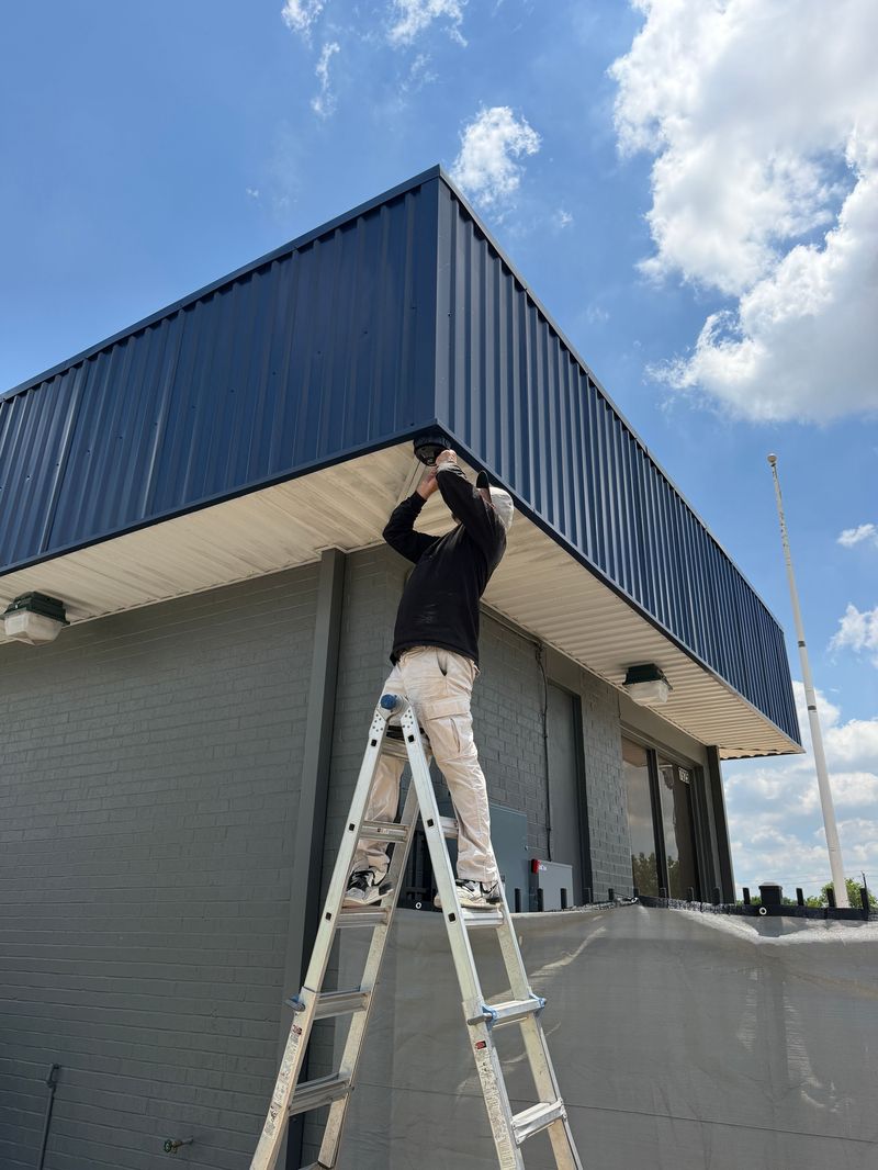 A SentryCam AI technician on a ladder installing an AI camera under the soffit of a commercial building.
